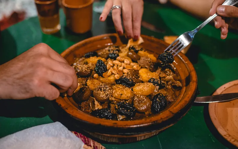 Convives qui se servent dans un tajine aux pruneaux, amandes et sésame