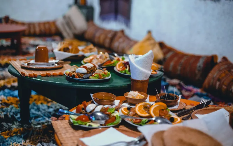 Tables basses garnies de salades marocaines et de tranches d’orange, dans une pièce bordée de coussins