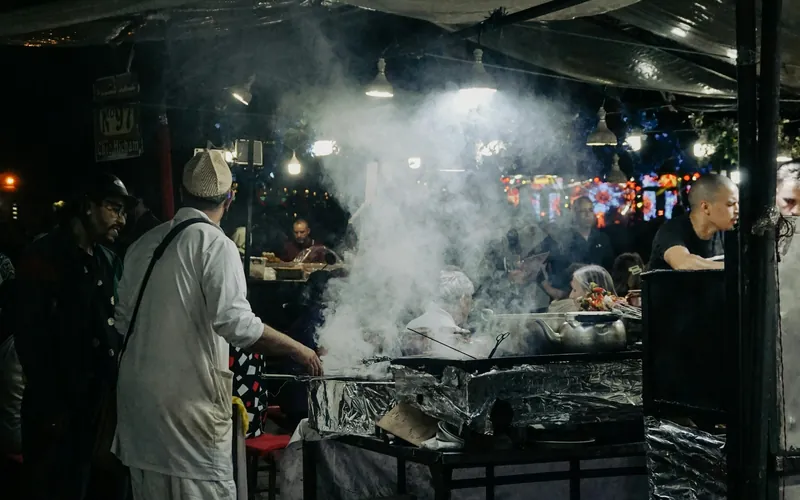 Cuisinier devant un grill fumant sous les lampes d’un stand de Marrakech, la nuit